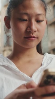 Kapatın, genç gülümseyen kadın yolun kenarında dururken cep telefonu kullanıyor.