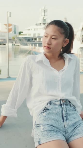 垂直ビデオ 港の桟橋で休んでいる若い女性 — ストック動画