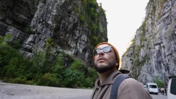 Muž cestovatel s batohem ve slunečních brýlích procházky na vysočinu po horské silnici. — Stock video