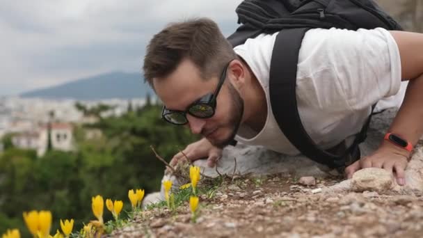 Mannelijke reizigers buigen voorover om bloemen te ruiken op rotsachtige heuvel. Rommelen bij het wandelen. — Stockvideo