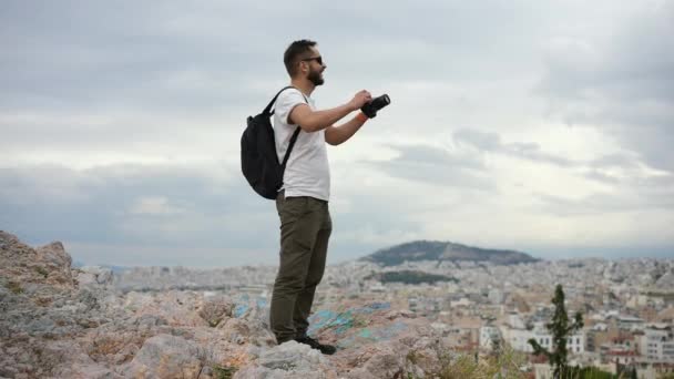 Turysta z kamerą w ręku stoi na wzgórzu i wyraża triumfalne uczucia. — Wideo stockowe