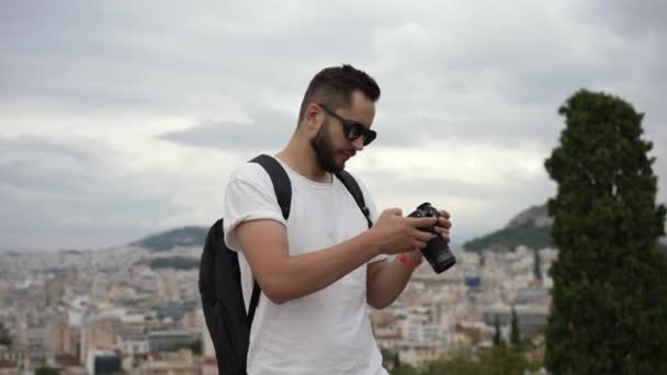 Portré a turisták srác nézi a kamerát álló sziklás dombon görög város. — Stock videók