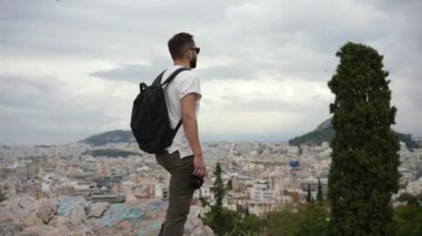 Yunan şehrindeki kayalık tepede bir turist kameraya bakar. Erkek gezginin portresi.