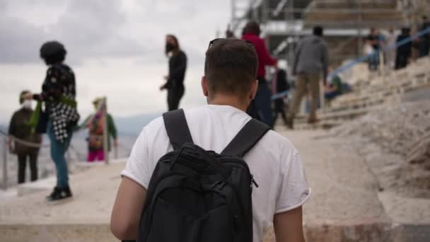 Viajante masculino entre a multidão de turistas caminha na colina da Acrópole, templo grego velho. — Vídeo de Stock