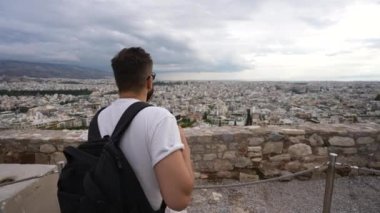 Gezgin adam Akropolis tepesinden modern Atina 'nın şehir manzarasına bakıyor.