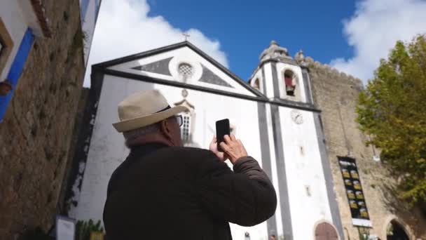 Äldre turist man i Fedora hatt ta bild, foto av gamla katolska stadskyrkan. — Stockvideo