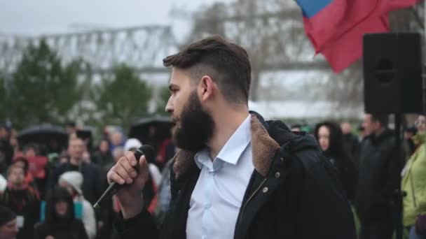 Male spokesperson on stage with mic gives address to crowd with Russian banners. — Stock Video