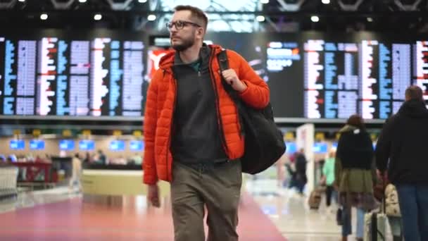 Ludzie na lotnisku. Mężczyźni w okularach z plecakiem spacerują pod szyldem. — Wideo stockowe