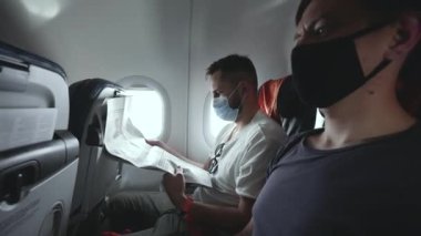 Uçağa binen yolcu, maskeli adam koltuğa oturur ve gazete okur.