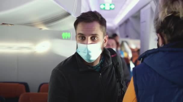 Egy maszkos arcú utas sétál a helyéhez a repülőn. Repülési tábla. — Stock videók