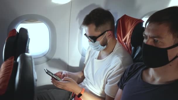 Pasażer w masce i okularach używa smartfona do rozmowy, smsowania w samolocie — Wideo stockowe