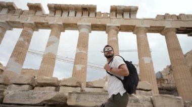 Gözlüklü gezgin Akropolis 'te yürüyor ve eski Yunan manzaralarına bakıyor..