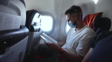 Koltuktaki maskeli yolcu kitap okuyor. Covid 19 salgınında yolculuk.