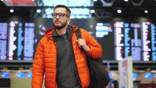 Pasajero masculino con mochila caminando en la terminal del aeropuerto debajo de la tabla de vuelo. — Vídeo de stock