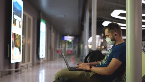 Pasajero masculino en mascarilla facial usando computadora portátil para esperar hasta el embarque en avión. — Vídeos de Stock