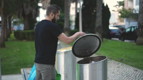 A férfi a szemetesbe dobja a borosüveget üveghulladéknak. Modern szemétválogatás. — Stock videók