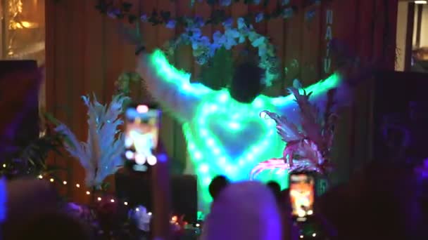 Pria DJ menari di panggung pertunjukan dengan mantel bulu putih dengan cahaya memimpin hati di belakang. — Stok Video
