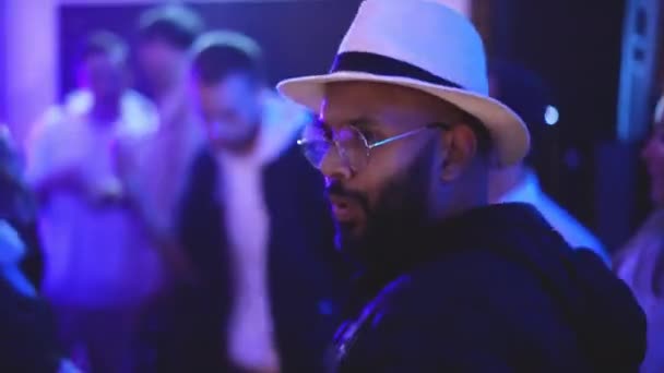Beyaz şapkalı Afrikalı adam gece kulübünde dans ederken hava öpücüğü yolluyor.. — Stok video