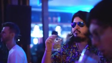 Uzun sakallı, gözlüklü, içki içen ve gece kulübü partisinde dans eden erkek.