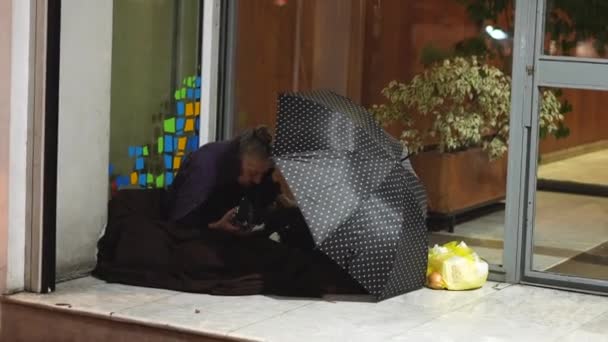 Starší šedovlasá bezdomovkyně sedí před obchodem. Starší lidé. — Stock video