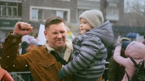 Single father with child on political rally, carrying kid with arm, waving fist. — Stock Video