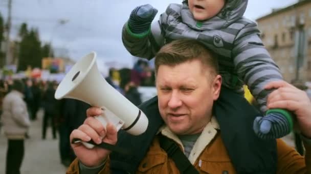Отец с мегафоном на мегафоне и сидящий мальчик на политической демонстрации. — стоковое видео