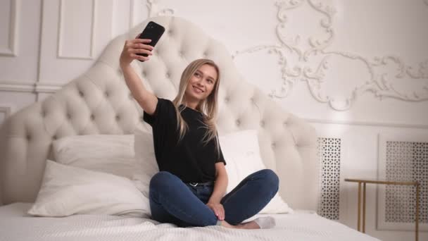 Hravá dáma nahrávat sama nebo fotit na telefonu sedí v ložnici. — Stock video