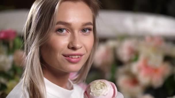 Primer plano retrato de encantadora chica rubia sonriente con flor mirando a la cámara. — Vídeos de Stock