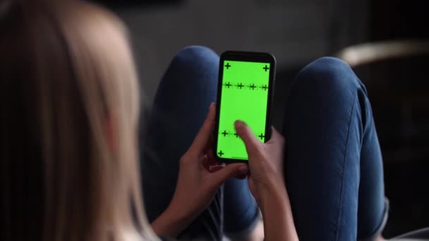 Dame est assise sur le canapé avec smartphone dans les mains. Écran vert chromakey mock up. — Video