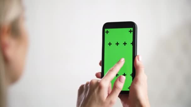 Fille tient dans les mains iphone et glisse, glisse vert maquette chromatique annonces écran. — Video