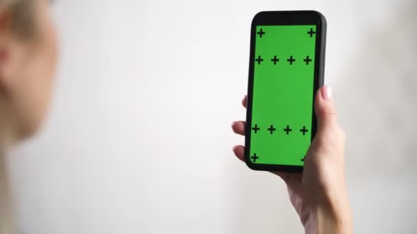 Fille tient dans les mains iphone et glisse, glisse vert maquette chromatique annonces écran. — Video