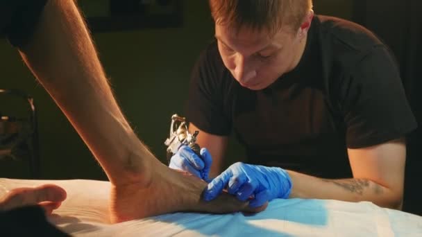 Татуювання в рукавичках з ретро-котушковою машиною фарбує клієнтів ногами з контуром чорнила . — стокове відео