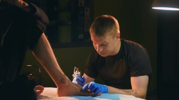 Maestro artista con bobina de la vieja escuela máquina colores pie tatuaje en la pierna de los clientes. — Vídeo de stock