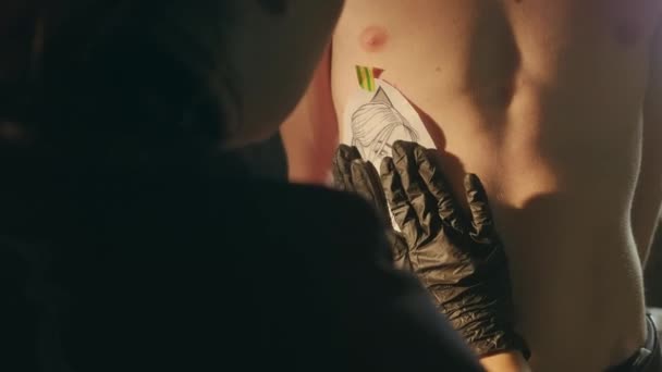 Carbon papier tatoeage kopiëren. vrouw tatoeëerder transfers meisjes gezicht op man borst. — Stockvideo