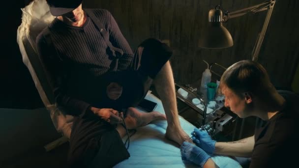 Болезненный взгляд на лица клиентов, в то время как татуировщик работает со старой рулонной машиной. — стоковое видео