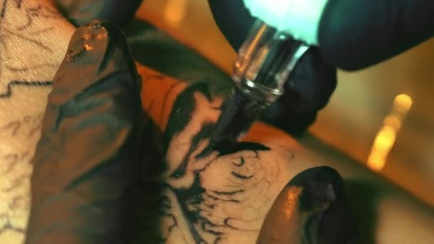 Tattoo kunstenaar in zwarte handschoenen met tatoeage pistool en tekening patroon contouren. — Stockvideo