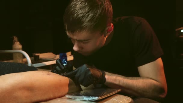 Cerca del trabajo de maestro tatuador. Dibujo esquema en la pierna, luz de la lámpara de trabajo. — Vídeo de stock