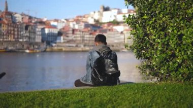 Asyalı trend siyah sırt çantalı turist Duero nehrinin rıhtımında tek başına oturuyor.