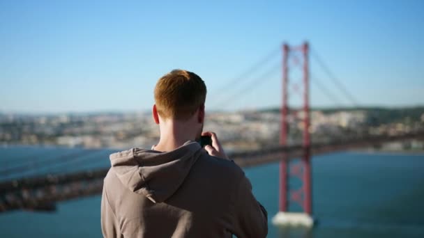 Viajando turista masculino com filmes de telefone marco da Ponte 25 de Abril em Lisboa. — Vídeo de Stock