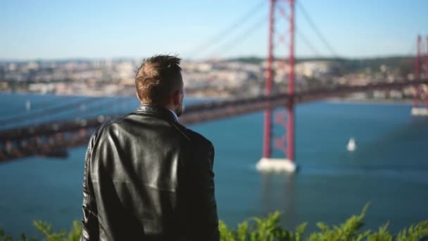 Alleenstaand mannelijk reizend toerist kijkt naar Lissabon stadsgezicht en Ponte 25 de Abril. — Stockvideo