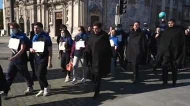 Siyah pelerinli son sınıf öğrencileri yeni öğrencilerle sokaklarda yürüyüp ilahiler söylüyor..