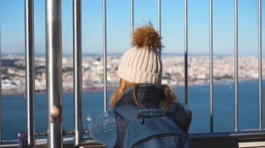 Kışın altında uzun saçlı kadın gezgin Cristo Rei heykel güvertesinde duruyor..
