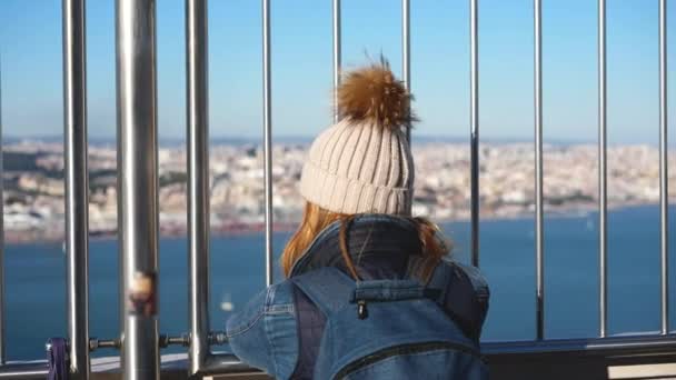 Vrouw reiziger met lang haar onder winterhoed staat op Cristo Rei standbeeld dek. — Stockvideo