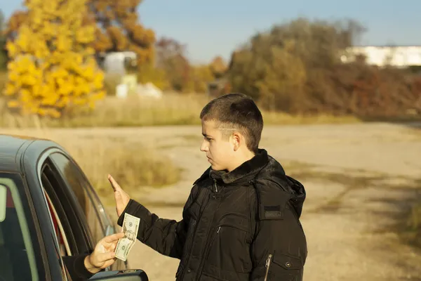 Alguien del coche está ofreciendo dinero al chico. —  Fotos de Stock