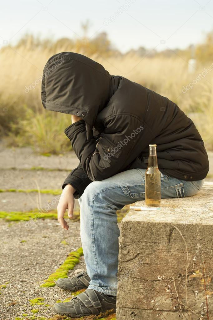 Boy with a bottle of drink, cigarettes and syringe in the foreground