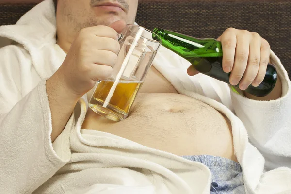 Uomo seduto sul divano con una birra nelle mani di — Foto Stock