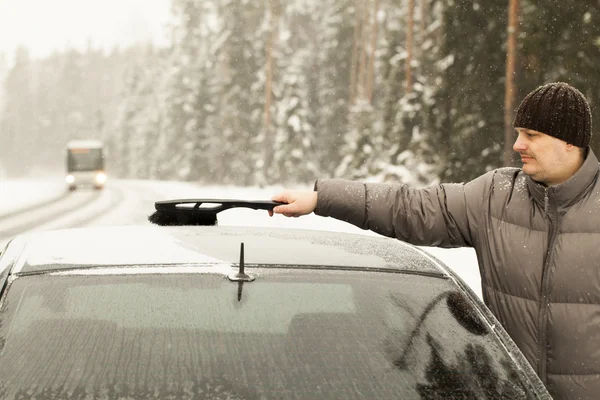 De mens reinigt de auto uit de sneeuw in de sneeuwstorm — Stockfoto