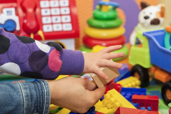 Mother and child hand on a multi colored toys background — Stock Photo, Image