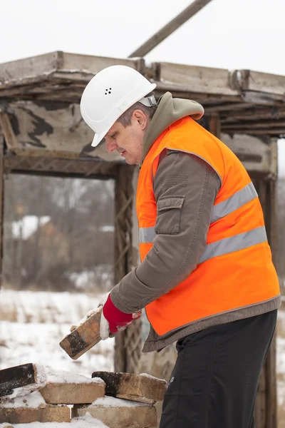 Trabalhador com tijolo nas mãos perto da casa velha queimada — Fotografia de Stock