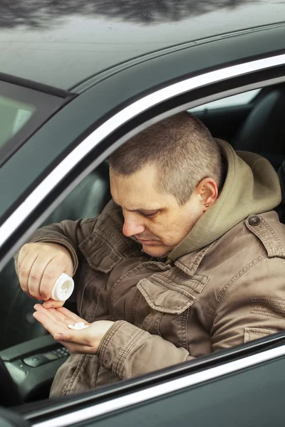 elinde ilaçlarla arabada oturan adam